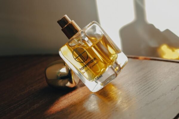 A clear glass perfume bottle with golden liquid on a wooden surface, softly lit.
